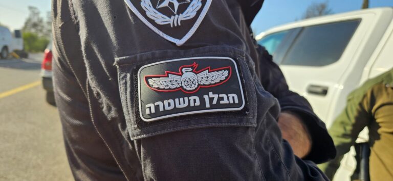 חבלן משטרה במדים מכופפים ליד פריט חשוד סמוך לבניין מגורים בנתניה, קלטת אזהרה צהובה מגדירה את הזירה, תושבים צופים ממרחק. פעולה זהירה ומדויקת עד לנטרול האמל״ח.