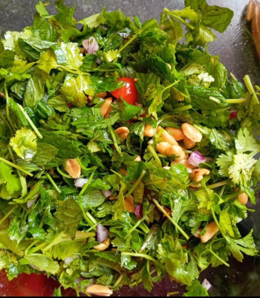 תמונה של סלט עלים טרי בקערה, עם עלי נענע, כוסברה ופטרוזיליה, בצל סגול, בוטנים וצ׳ילי. הצבעים ירוקים ורעננים, והסלט מצולם מזווית עליונה, במראה קליל ולא מתאמץ - בדיוק כמו מתכון שנולד מרגע ספונטני במטבח.