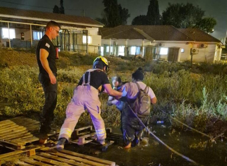 לוחמי אש עומדים בשטח בוצי באתר עבודות ביוב בראש העין, כשהם מושכים בחבל אישה שחולצה מבור טובעני