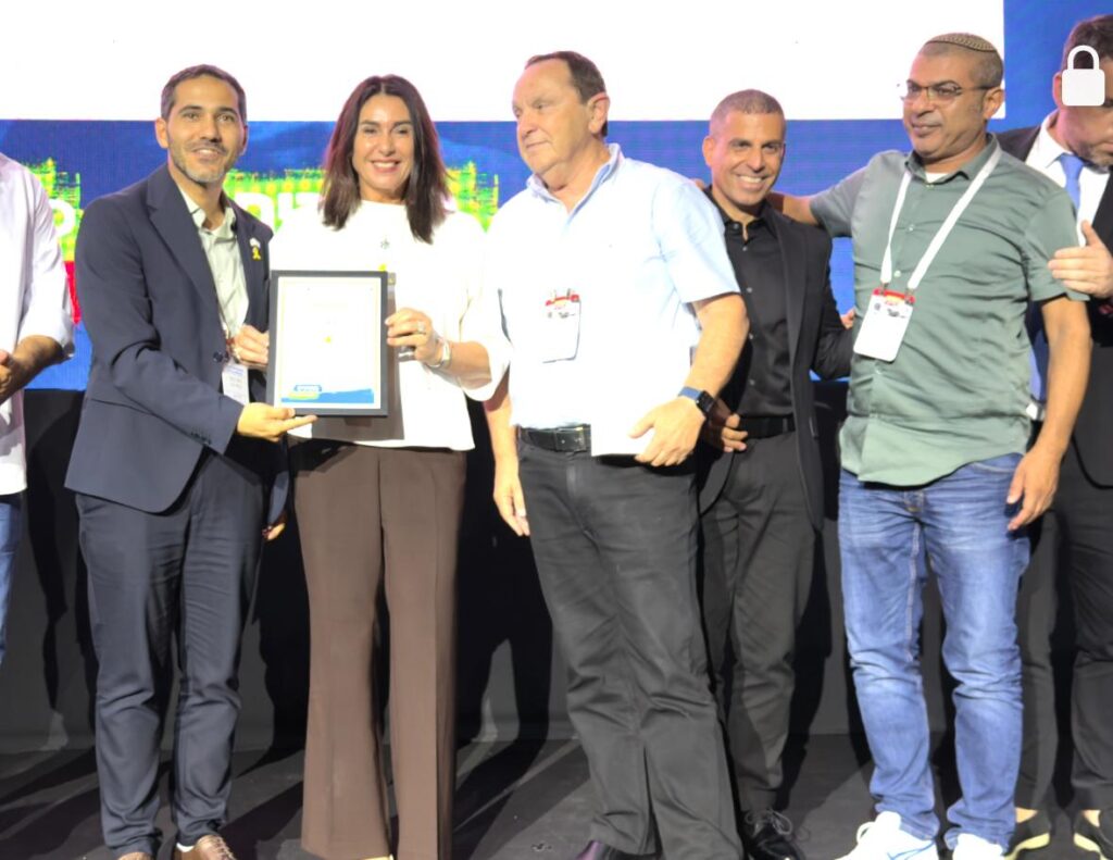 שרת התחבורה מירי רגב מעניקה לראש העיר רועי גבאי את מגן ההצטיינות על הבמה; גבאי מחזיק את המגן בגאווה, נציגי יבנה עומדים סביבו ומוחאים כפיים. רגע של ניצחון עירוני וקהילתי.