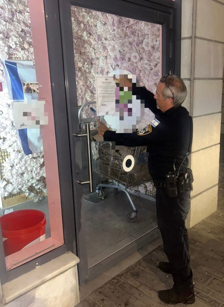 שוטר תחנת ראש העין מדביק צו סגירה על דלת העסק במהלך הפעילות