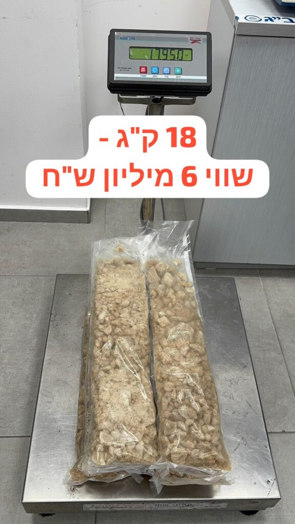 בודקי מכס ובלשי משטרה פותחים מזוודה על שולחן בדיקה; בתוך הדופן הכפולה נראות שקיות אטומות עם החומר החשוד כסם. הצילום בזמן אמת