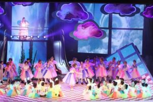 בני נוער על במה ענקית, עטופים באור ובצבע, רגע לפני שמתחילים את מסע הקסם של "אליס בארץ הפלאות", מתוך שנים עברו