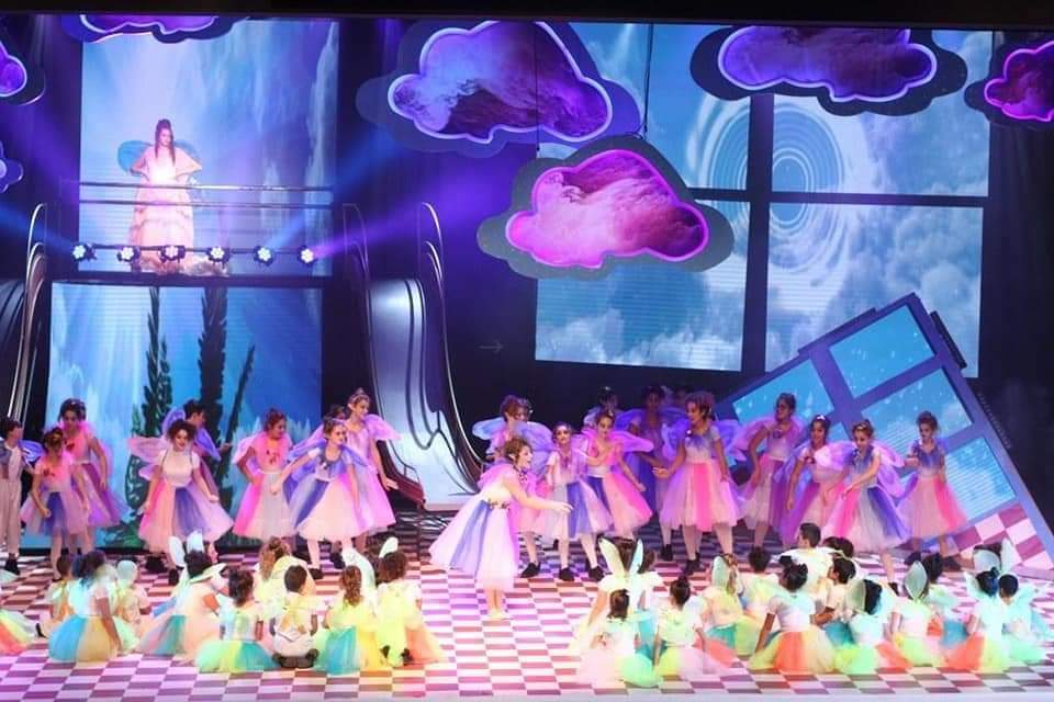 בני נוער על במה ענקית, עטופים באור ובצבע, רגע לפני שמתחילים את מסע הקסם של "אליס בארץ הפלאות", מתוך שנים עברו