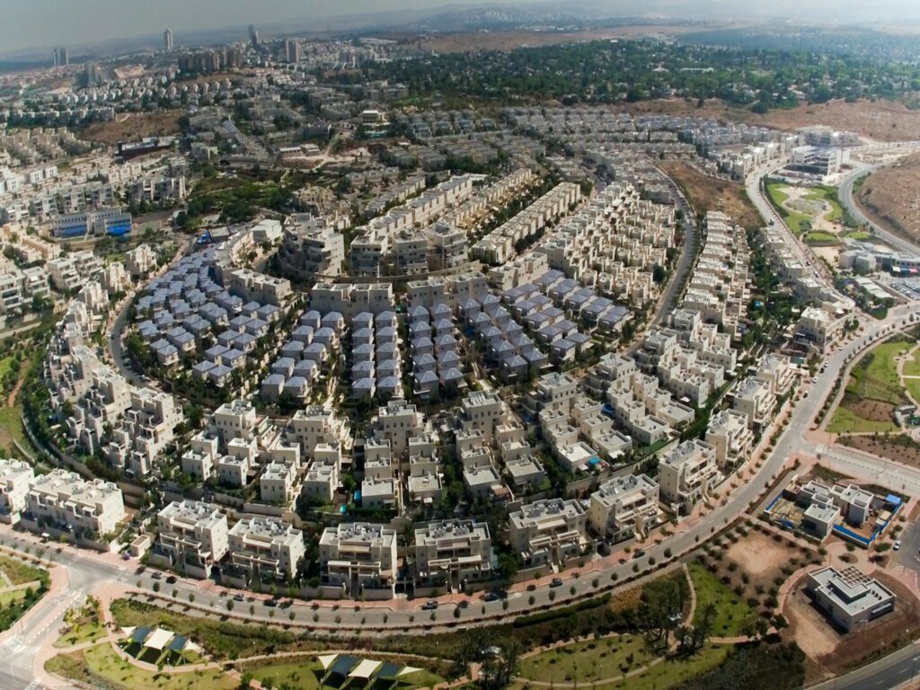 נוף פנורמי של מודיעין מכבים רעות עם פארקים ירוקים, שכונות חדשות ותושבים בפעילות קהילתית וספורטיבית.
