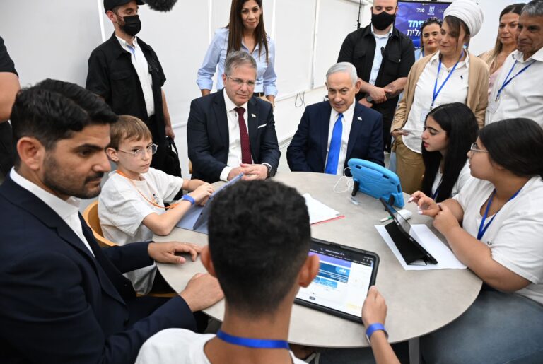 תלמידים בכיתת לימוד דיגיטלית עובדים מול מחשבים וטאבלטים לצד מורה, במסגרת שיעור אנגלית המבוסס על בינה מלאכותית ולמידה מותאמת אישית.