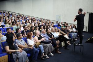 קהל גדול באולם תרבות ברמלה צופה במופע בידור חגיגי, כשברקע אווירה חמה של ערב הוקרה למשפחות המילואים והקבע