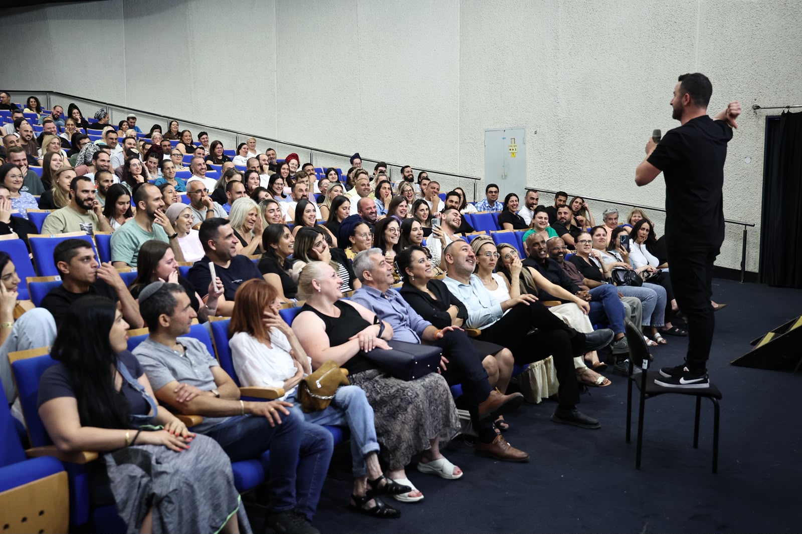 קהל גדול באולם תרבות ברמלה צופה במופע בידור חגיגי, כשברקע אווירה חמה של ערב הוקרה למשפחות המילואים והקבע