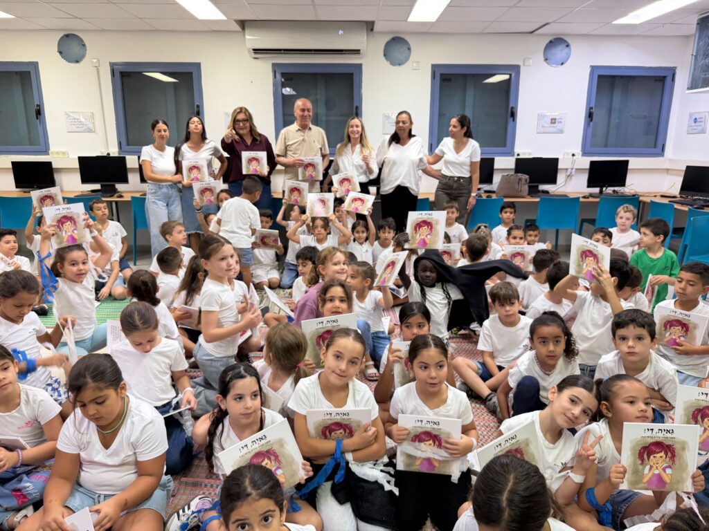 ראש עיר מקריא סיפור לתלמידי כיתה א' היושבים במעגל בכיתה צבעונית, כשכל ילד מחזיק בידו ספר חדש שקיבל לקראת חופשת הקיץ