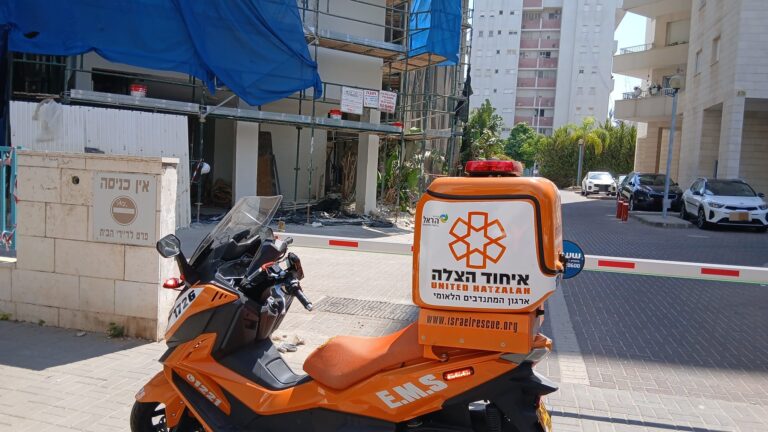 צוותי רפואה מעניקים טיפול ראשוני לפועל באתר בנייה ברחוב עירוני, כשברקע שלד מבנה, פיגומים וכלי עבודה.