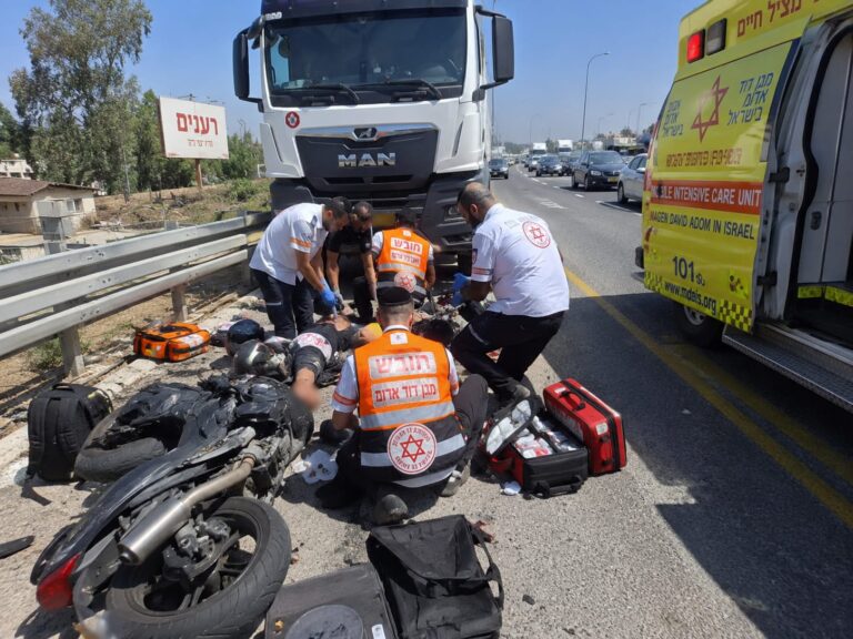 כוחות הצלה ורפואה מעניקים טיפול לרוכבי אופנוע לצד כביש ראשי סמוך ליהוד, כשברקע משאית וניידות חירום בזירת התאונה