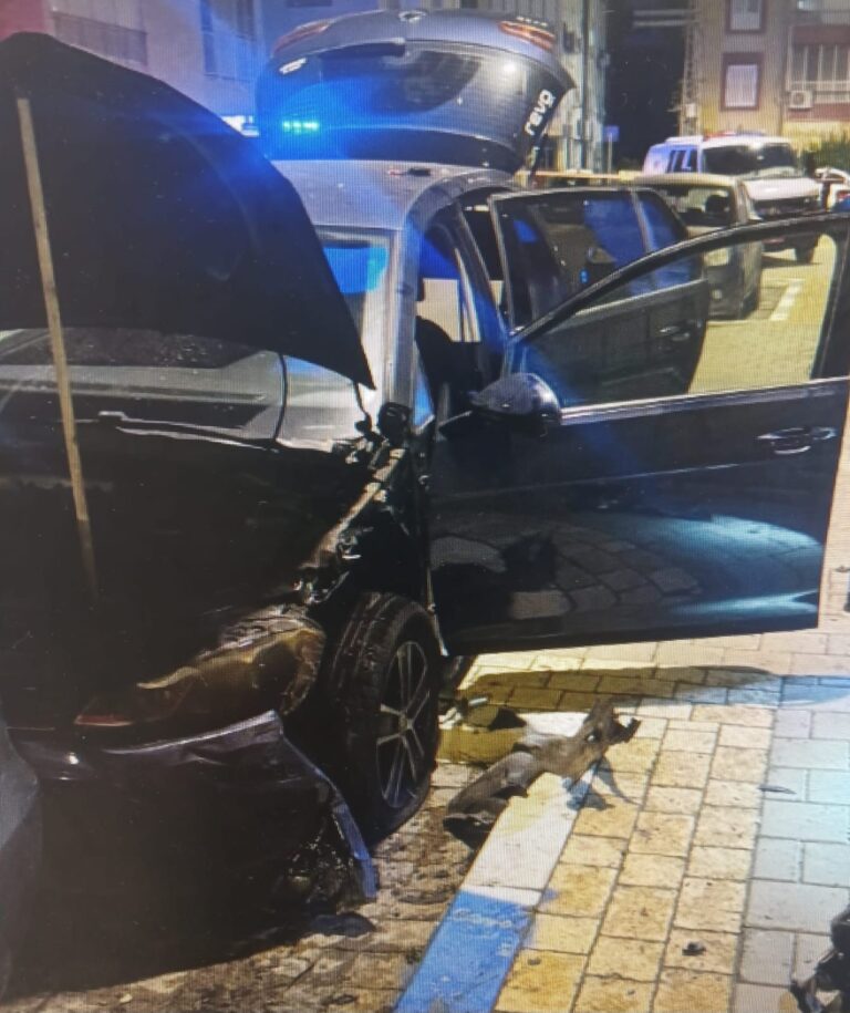 רכב שניזוק בפיצוץ עומד ברחוב עירוני, כששוטרים וחבלני משטרה פועלים בזירה ומרחיקים את האזור לבדיקה