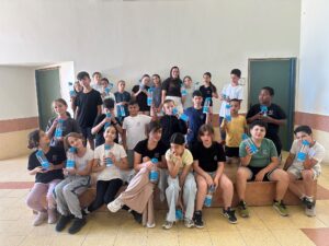 תלמידי בית ספר בגן יבנה עובדים יחד על כרזות צבעוניות בנושא שמירה על המים, כשברקע מוצגים ציורים, טיפות מים וסיסמאות סביבתיות שיצרו בעצמם
