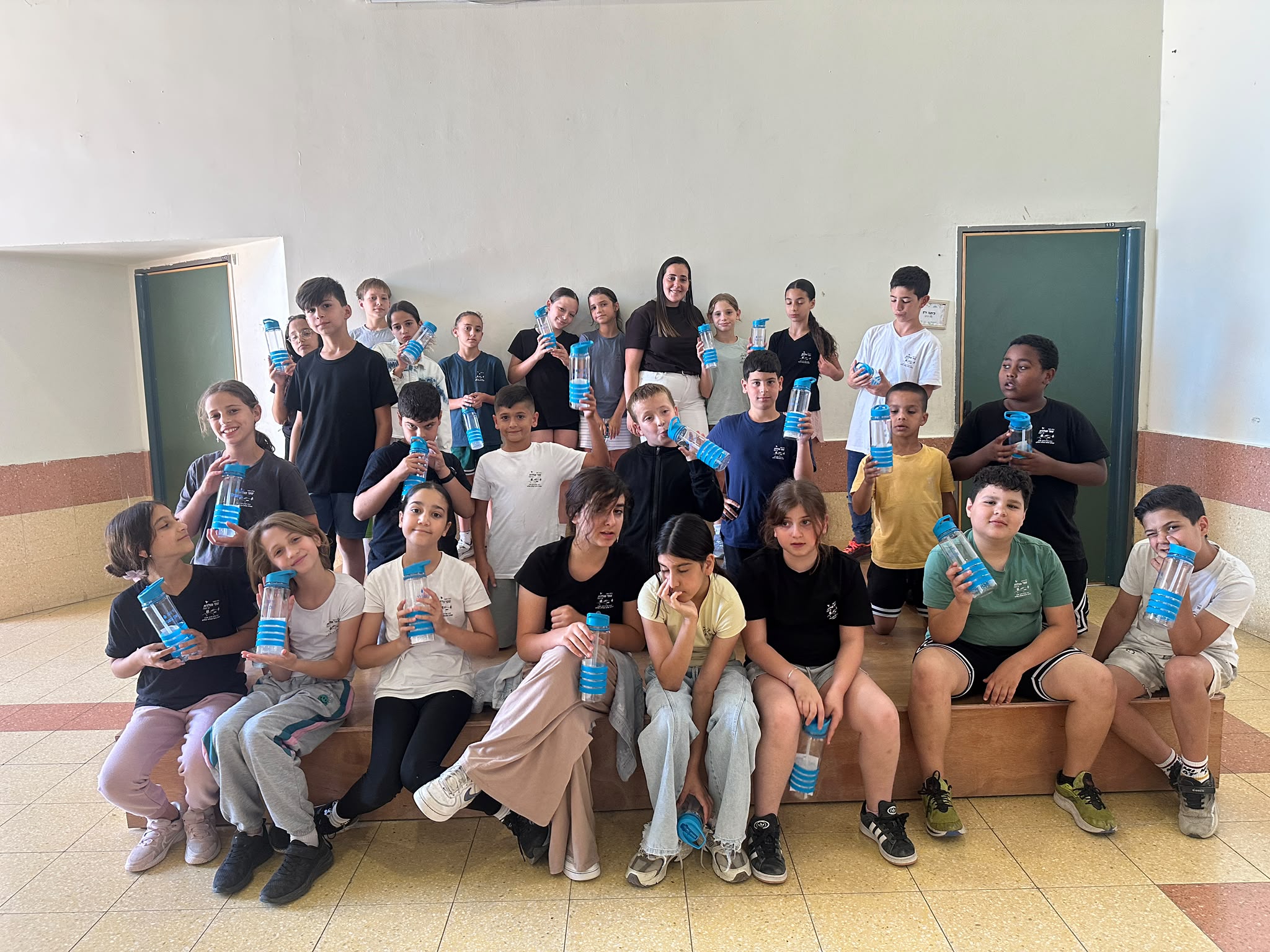תלמידי בית ספר בגן יבנה עובדים יחד על כרזות צבעוניות בנושא שמירה על המים, כשברקע מוצגים ציורים, טיפות מים וסיסמאות סביבתיות שיצרו בעצמם