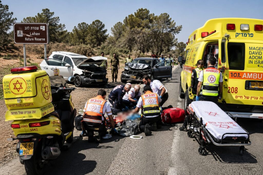 כוחות הצלה פועלים בזירת תאונת דרכים בכביש בדרום, סמוך לאזור מיוער ופתוח, עם כלי רכב שנפגעו וצוותי מד"א בזירה