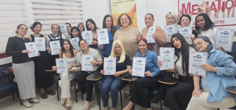 מחנכות ומטפלות עומדות יחד בטקס סיום קורס הכשרה לגיל הרך, מחזיקות תעודות ומחייכות לצד נציגי אגף החינוך