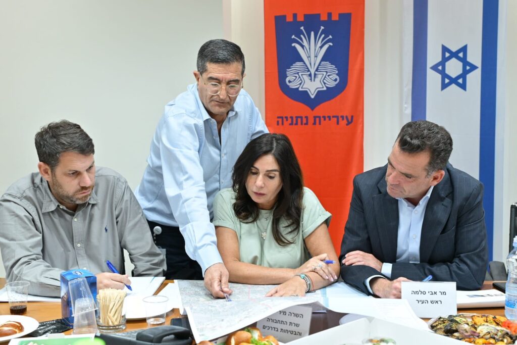 תחנת רכבת עירונית בנתניה לצד אוטובוסים, שביל אופניים וציר תנועה מרכזי, כשברקע שכונות מגורים חדשות ומרחב עירוני מתפתח