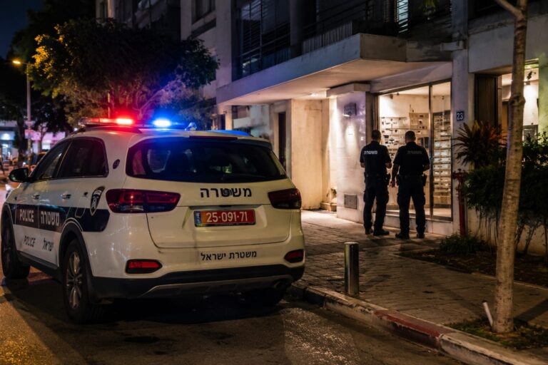 ניידת משטרה עומדת ברחוב עירוני בתל אביב בשעות הערב, סמוך לבניין מגורים שבו מתנהלת חקירה