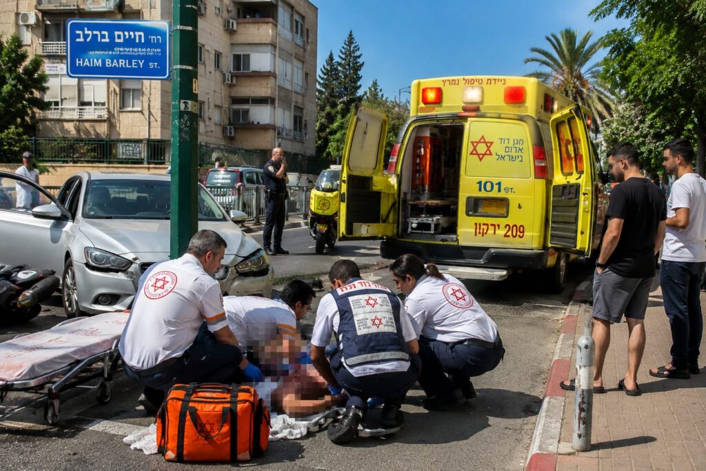 זירת תאונת דרכים ברחוב עירוני, כוחות מד"א מעניקים טיפול רפואי להולך רגל מבוגר סמוך לניידת אמבולנס, כאשר כוחות החירום פועלים במקום