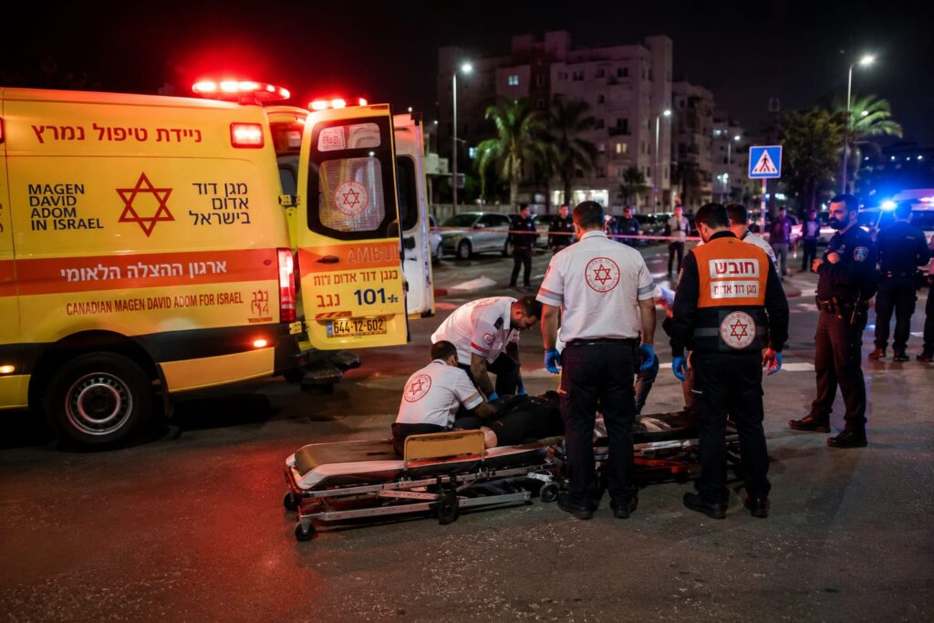 ניידת טיפול נמרץ של מד"א וכוחות חירום בזירת אירוע בעיר בשעות הלילה, כאשר צוותים רפואיים מעניקים טיפול לפצוע ומבצעים פעולות פינוי לבית החולים