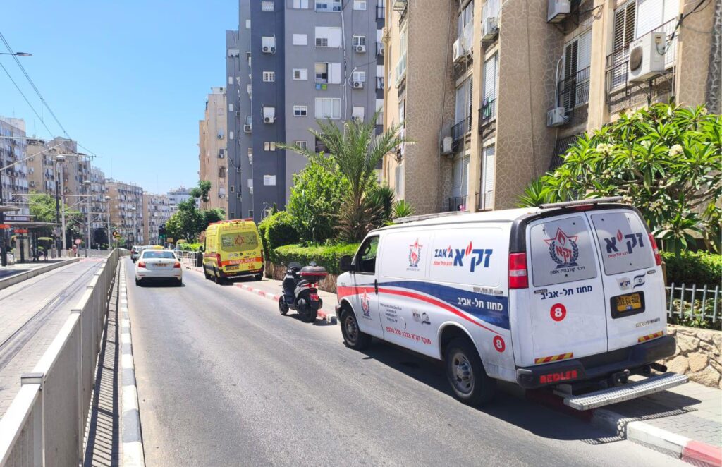 בניין מגורים ברחוב עירוני בבת ים, עם ניידת חירום וצוותי סיוע הפועלים סמוך לכניסה לבניין.