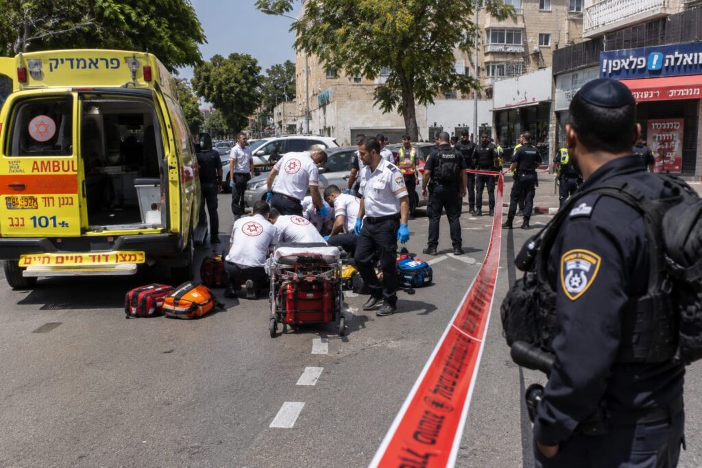 כוחות מד"א ומשטרה פועלים בזירת אירוע אלימות ברחוב עירוני ברמלה, לצד ניידת טיפול נמרץ וסרטי סימון בזירה