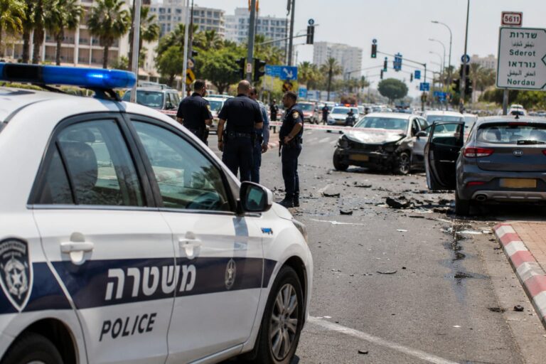 ניידת משטרה בזירת תאונת דרכים בכביש עירוני בנתניה, כששוטרים חוקרים את האירוע ורכבים פגועים עומדים בצד הדרך