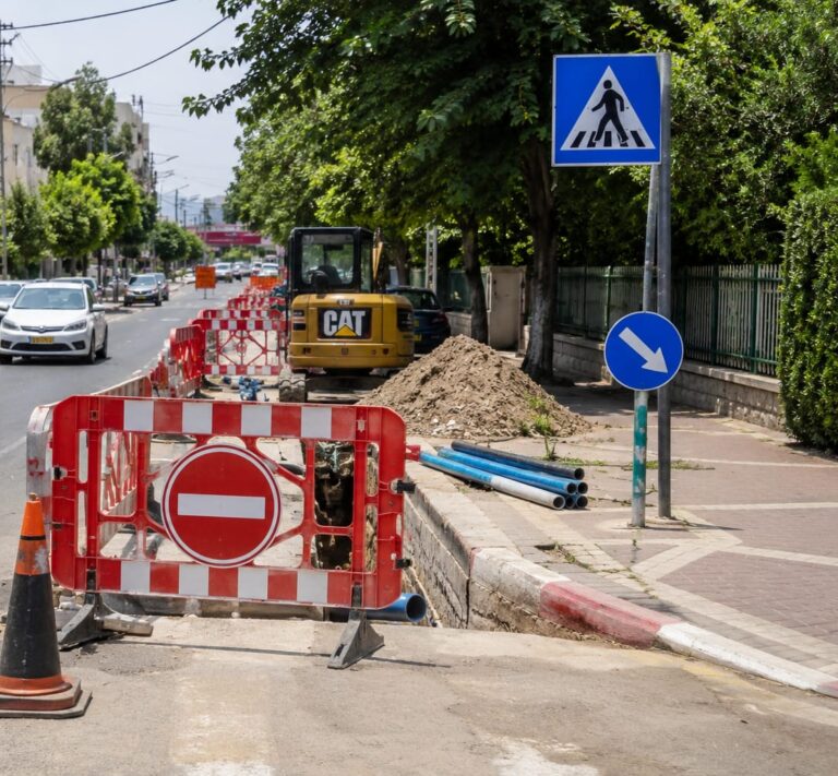 עבודות תשתית ברחוב עירוני ברחובות, עם שילוט הכוונה ותנועת הולכי רגל לצד המדרכה