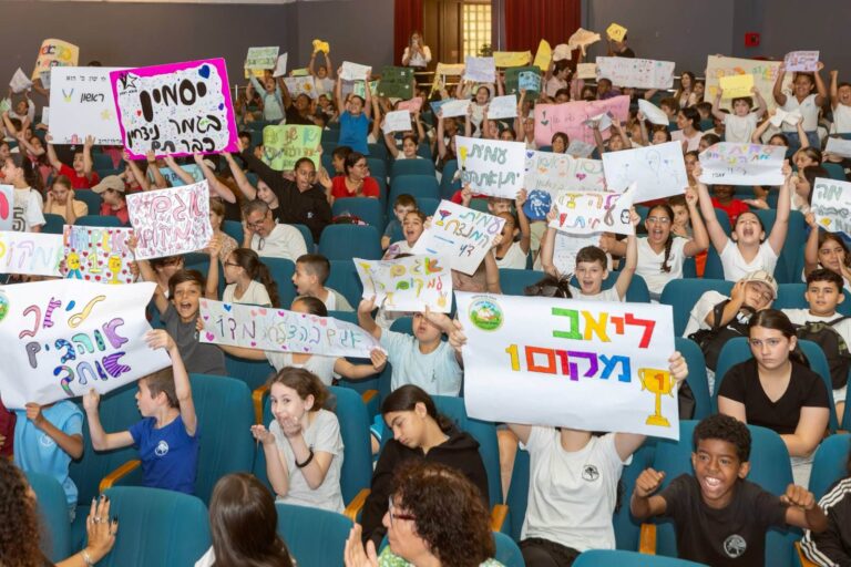 תלמידות ותלמידים באשקלון משתתפים בחידון קיימות עירוני, עומדים על במה או באולם בית ספר עם תעודות, לצד נציגי העירייה וצוותי החינוך