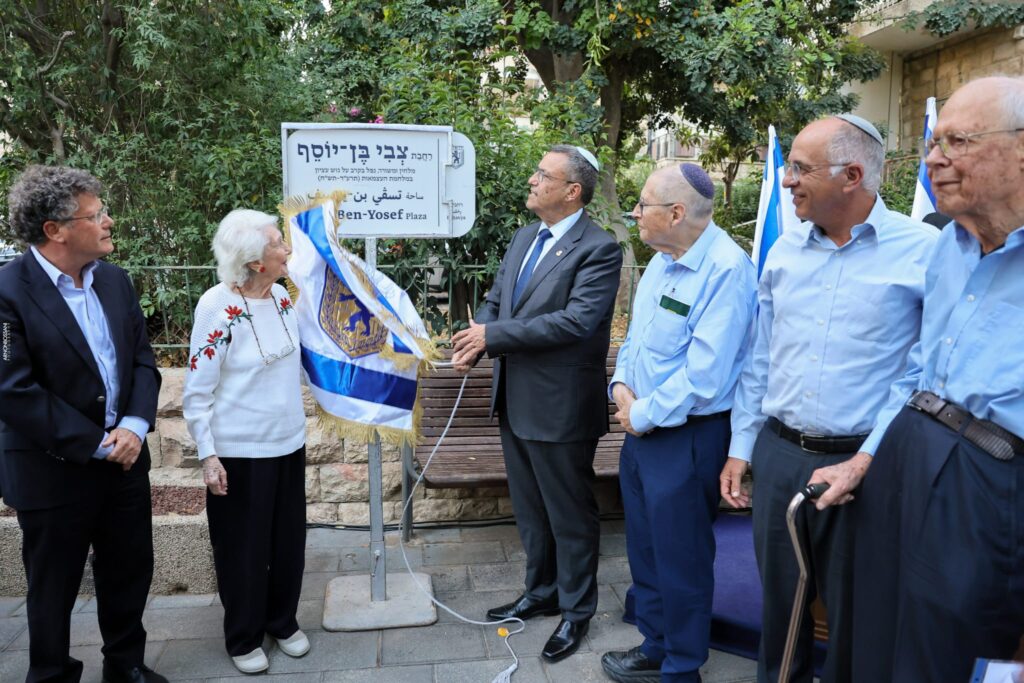 טקס חנוכת רחבה חדשה בשכונת רחביה בירושלים, עם שלט הנצחה, נציגי העירייה, מוקירי זכרו ותושבים, באווירה מכובדת של זיכרון, תרבות והיסטוריה עברית