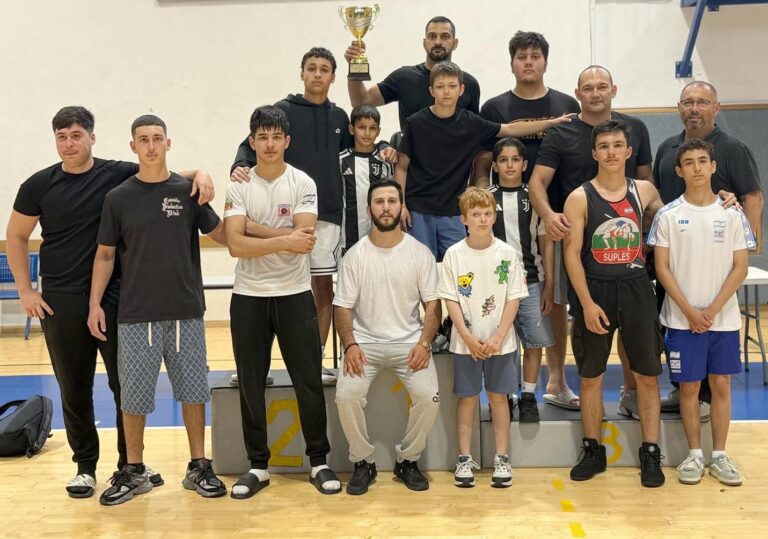 ספורטאים וספורטאיות מלוד מניפים גביעים ומדליות בטקס חגיגי. ברקע שחקני כדורסל, מתאבקים ומתאגרפים, לצד קהל מעודד ואווירת ניצחון וגאווה עירונית