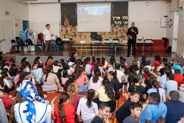 תלמידים מראש העין מסיירים לאורך נחל רבה, מחזיקים דפי תצפית וזכוכיות מגדלת, מתבוננים בצמחייה ובמים, ולומדים על שמירת טבע במרחב העירוני