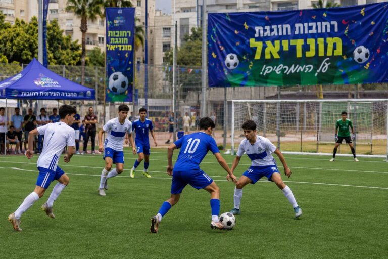 ילדים, בני נוער ומבוגרים משתתפים בטורניר כדורגל קהילתי במגרש ספורט ברחובות באווירת מונדיאל