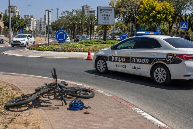 זירת תאונת דרכים במעגל תנועה באזור השרון, עם ניידת משטרה ואופניים חשמליים בצד הדרך.