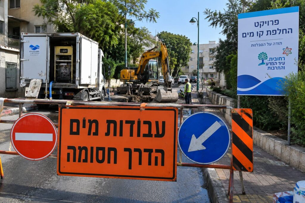 עבודות תשתית להחלפת קו מים ברחוב עירוני, לצד כלי עבודה ותמרורי הכוונה זמניים באזור מגורים