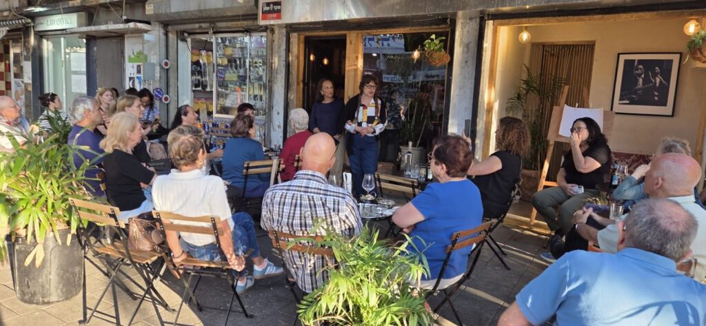קבוצת אזרחים ותיקים יושבת בבר תל אביבי באווירה שמחה וחברתית במהלך ערב הרצאה ותרבות