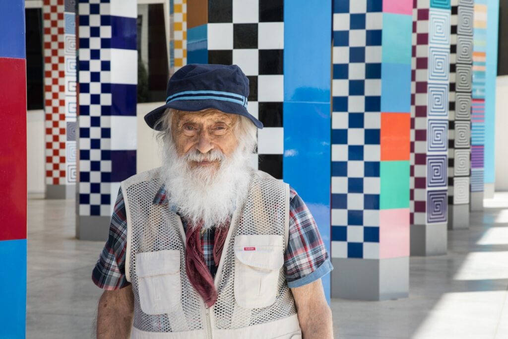 יעקב אגם לצד אחת מיצירותיו הצבעוניות והקינטיות במוזיאון אגם בראשון לציון