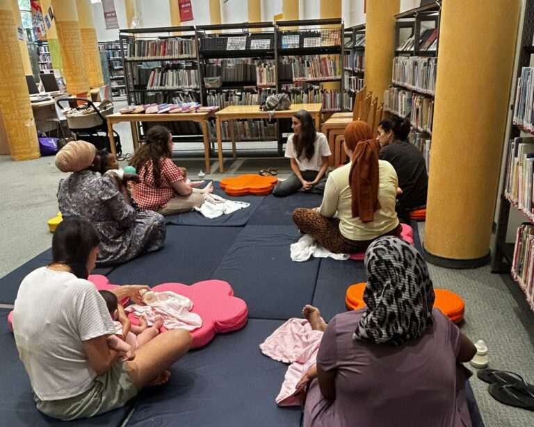אם יושבת עם תינוק קטן ומקריאה לו ספר צבעוני במהלך פעילות משותפת לקידום שפה ותקשורת
