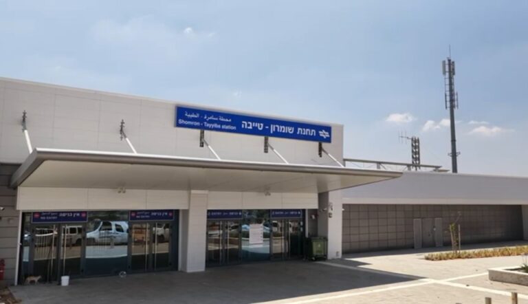 רכבת נוסעים חולפת על מסילה חדשה לצד תחנת רכבת מודרנית