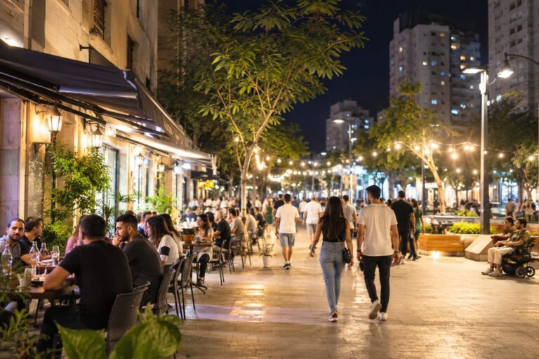 אזור מסחר פעיל ביבנה בשעות הערב, עם בתי עסק פתוחים ותושבים מבלים במרחב העירוני