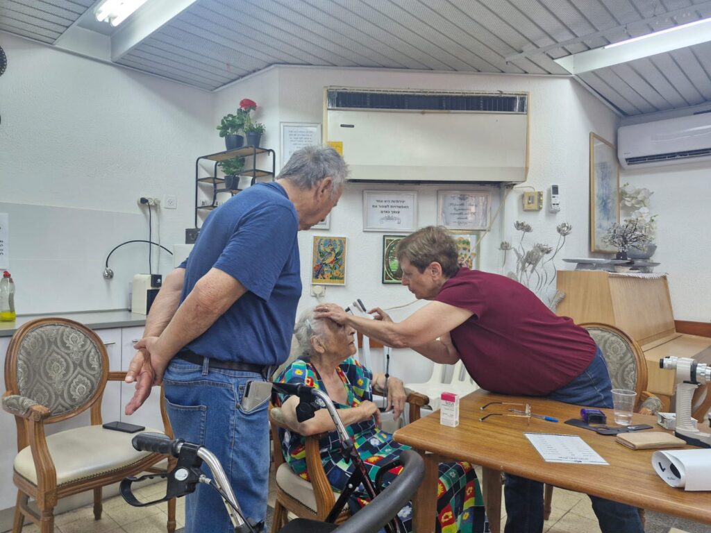 ד״ר חיה זהבי מבצעת בדיקת עיניים לשורדי שואה בבית דיור עמידר ביהוד במסגרת פעילות עמותת “למענם”