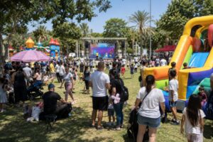 משפחות וילדים נהנים מאירוע קיץ צבעוני בפארק ברמלה עם מתנפחים, במה ואטרקציות ברקע.