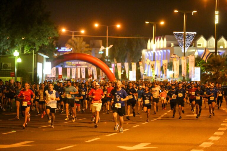 מרוץ לילה מואר בפארק הנחל בבאר שבע, עם רצים לאורך המסלול וקהל מעודד