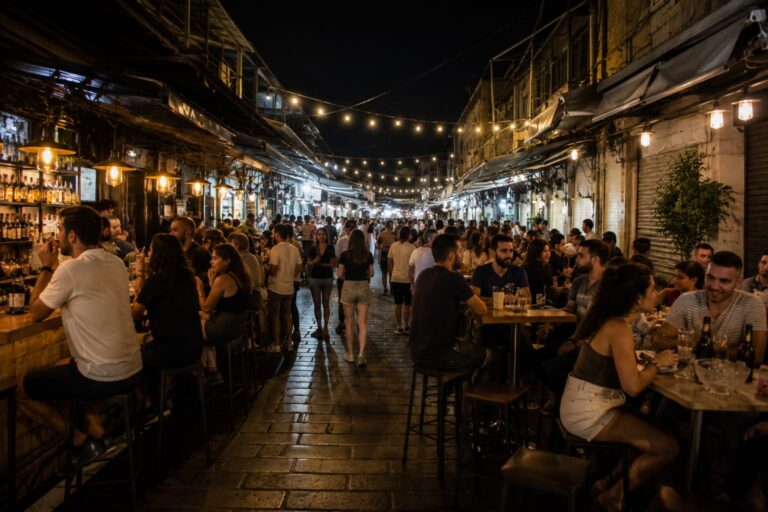 צילום לילי של הברים והשולחנות בשוק מחנה יהודה, לצד מבקרים במרחב הציבורי