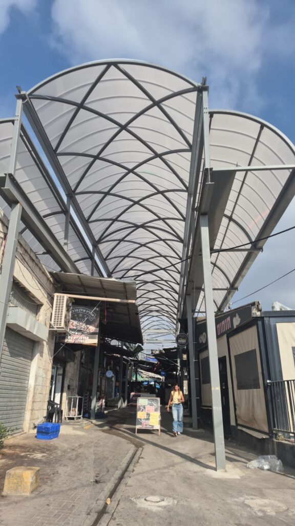 התקנת לוחות הקירוי מעל דוכני שוק רמלה בזמן שהמסחר ממשיך לפעול