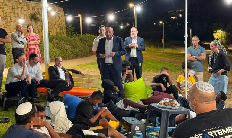 : צילום של בני נוער יושבים על מחצלות בפארק בשעות הערב לצד אנשי מקצוע, עם משחקי חברה ואווירה קהילתית