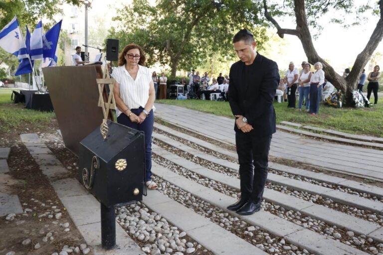 אנדרטת הזיכרון בשכונה ט' בבאר שבע עם נרות זיכרון, דגלי ישראל ומשתתפי הטקס עומדים בדקת דומייה
