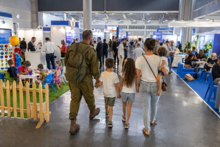 משפחת מילואימניק נכנסת לאקספו תל אביב, כשברקע דוכני חברות, נציגי מעסיקים, מתחם פעילות לילדים ואווירת יריד תעסוקה משפחתי