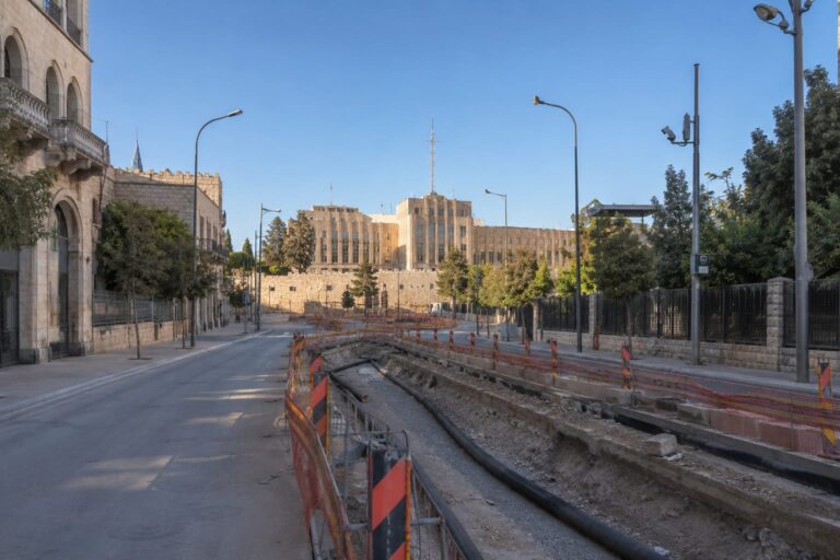 רחוב מרכזי בירושלים עם אתר עבודות תשתית שקט וללא פעילות, כשברקע בניין עיריית ירושלים ואווירת יום צום