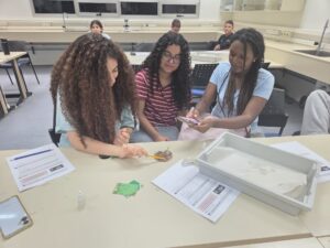 קבוצת תלמידים ותלמידות במעבדת מדע מתקדמת במכון ויצמן, לצד רובוט לימודי ומסכי מחשב, באווירת חדשנות ומצוינות